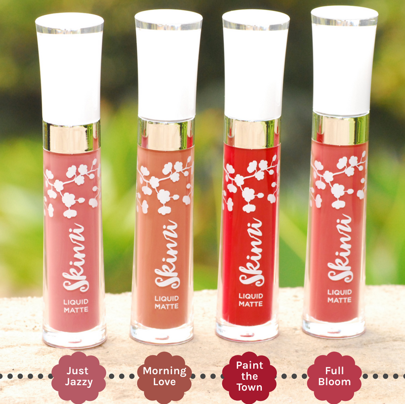 Image of 4 Skinzi Liquid Mattes on top of a stone wall overlooking a green grassy field, with Just Jazzy showing first followed by Morning Love, Paint The Town and Full Bloom. The labels are also specified under each lipstick shade.